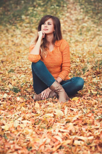 Porträt einer denkenden Frau in Jeans und Pullover in der Natur, die auf gelben Herbstblättern sitzt — Stockfoto