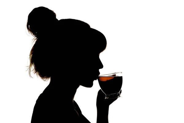 Silhouettenprofil einer schönen Frau, die heißen schwarzen Tee aus einer gläsernen transparenten Tasse trinkt, ein unkenntlich gemachtes Mädchengesicht auf weißem, isoliertem Hintergrund, ein Konzept der Entspannung — Stockfoto