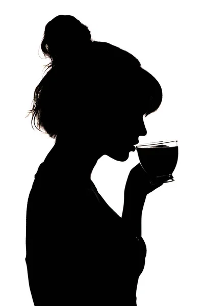 Silhouettenprofil einer schönen Frau, die heißen schwarzen Tee aus einer gläsernen transparenten Tasse trinkt, ein unkenntlich gemachtes Mädchengesicht auf weißem, isoliertem Hintergrund, ein Konzept der Entspannung — Stockfoto