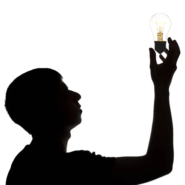 Silhouette of thoughtful man holding in hand the incandescent glowing lamp upwards, thought bulb, concept of idea on white isolated background — Stock Photo, Image