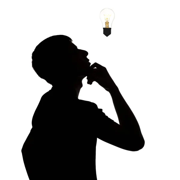 Silhouette of thoughtful man looking at the incandescent lamp upwards, thought bulb, concept of idea on white isolated background — Stock Photo, Image