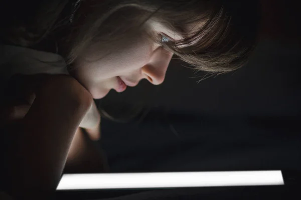 The face of a young woman lighted by a tablet screen light, the — Stock Photo, Image