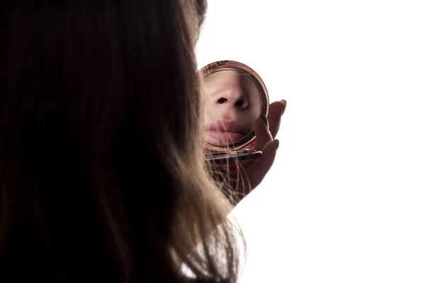 Отражение молодой красивой женщины на белом изолированном фоне, лицо женщины, смотрящей в карманное зеркало, концепция красоты и моды — стоковое фото