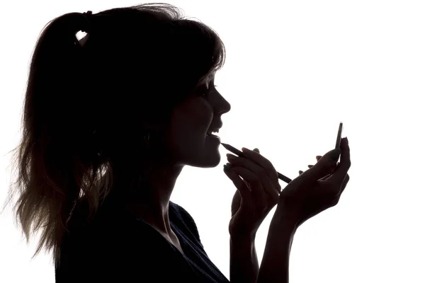 Silueta de la mujer haciendo maquillaje delante del espejo de bolsillo en las manos sobre fondo blanco aislado — Foto de Stock