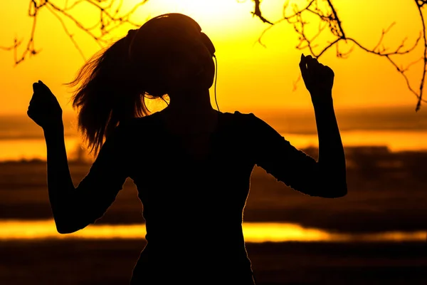夕日に音楽を楽しんでいる女の子、ヘッドホンを女性のシルエット — ストック写真