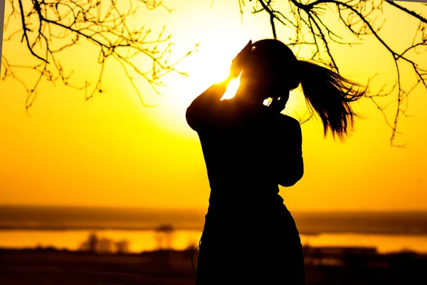 Silhouette d'une femme dans les écouteurs, la fille jouissant de la musique sur le coucher du soleil — Photo
