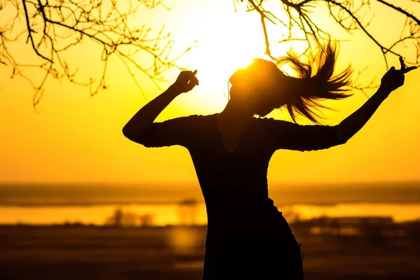 Silhueta de uma mulher em fones de ouvido, a menina desfrutando de música no pôr do sol — Fotografia de Stock