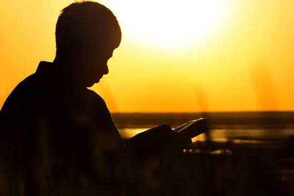Silhueta de um homem lendo a Bíblia no campo, o homem orando a Deus na natureza, o conceito de religião e espiritualidade — Fotografia de Stock
