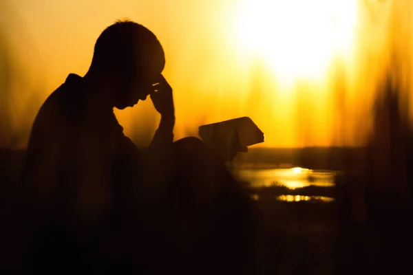 Силуэт молодого человека с Библией, мужчина, молящийся Богу в природе, понятие религии и духовности — стоковое фото