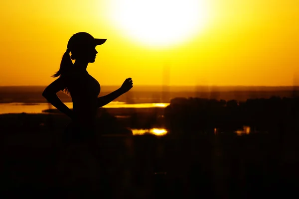 Силуэт женщины, бегающей по природе на закате, спортивный женский профиль, концепция спорта и досуга — стоковое фото