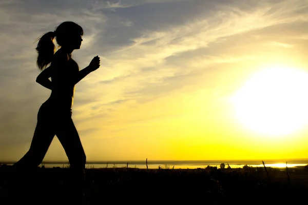 Silhueta de uma mulher correndo sobre a natureza ao pôr do sol, esportes perfil feminino, conceito de esporte, lazer e cuidados de saúde — Fotografia de Stock
