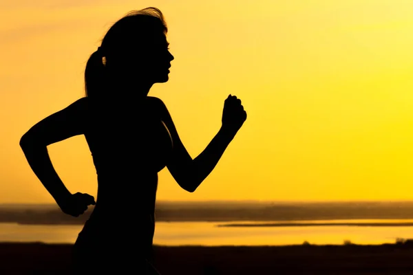 Σιλουέτα μιας γυναίκας τρέξιμο στη φύση στο ηλιοβασίλεμα, αθλητικά γυναικεία προφίλ, έννοια του αθλητισμού, αναψυχής και υγειονομική περίθαλψη — Φωτογραφία Αρχείου