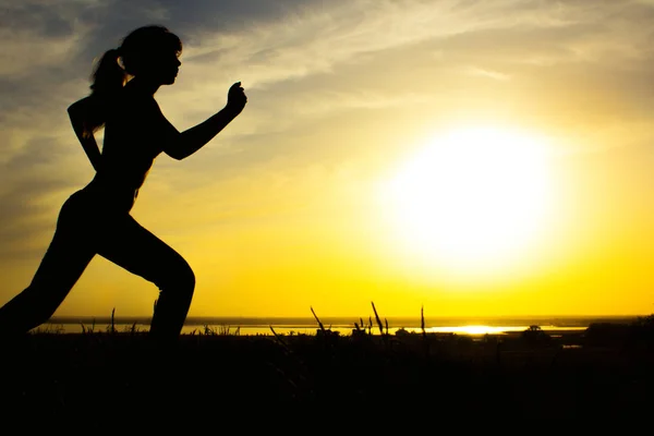 Silhueta de uma mulher correndo sobre a natureza ao pôr do sol, esportes perfil feminino, conceito de esporte, lazer e cuidados de saúde — Fotografia de Stock