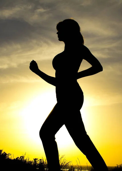 Silhouette di una donna che fa jogging sulla natura al tramonto, profilo sportivo femminile, concetto di sport, tempo libero e salute — Foto Stock