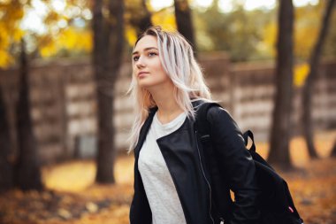 Güz parkında doğa üzerinde yürüyen güzel, şık bir kızın portresi, açık havada günlük giysiler içinde genç bir kadın.