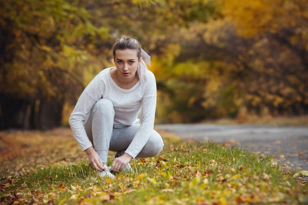 アスファルト道路上の白いスニーカーに靴ひもを結ぶためにスクワット女の子,屋外秋のスポーツの概念 — ストック写真