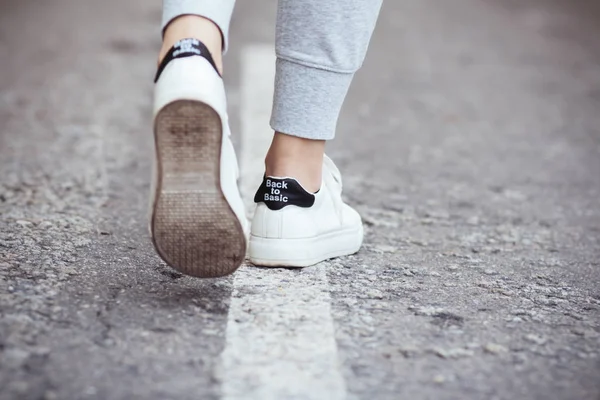 Pieds d'une jeune femme dans une sneaker blanche faisant un pas sur un asphalte, concept de sport et de soins du corps — Photo