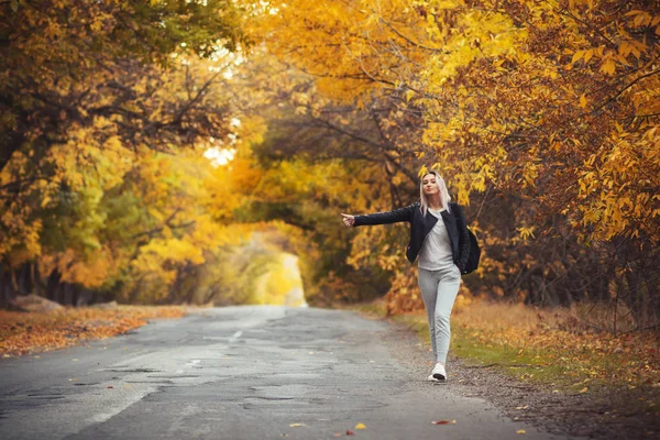Junge Frau steht und wartet bei kaltem Herbstwetter auf einer asphaltierten Straße, ein Mädchen versucht, mit einer Handbewegung von einer Vorstadtautobahn zu kommen — Stockfoto