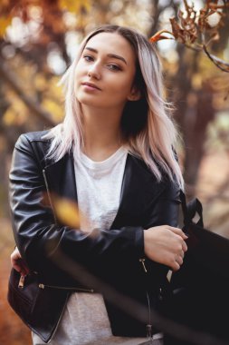 Güz parkında doğa üzerinde yürüyen güzel, şık bir kızın portresi, açık havada günlük giysiler içinde genç bir kadın.