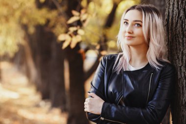 Ağaç gövdesine dayanmış güzel bir kızın portresi. Sonbahar parkında doğa üzerine yürüyen genç bir kadın.