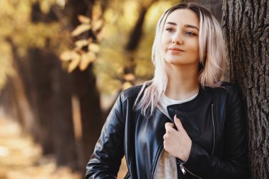 Ağaç gövdesine dayanmış güzel bir kızın portresi. Sonbahar parkında doğa üzerine yürüyen genç bir kadın.