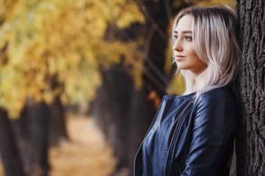 Ağaç gövdesine dayanmış güzel bir kızın portresi. Sonbahar parkında doğa üzerine yürüyen genç bir kadın.