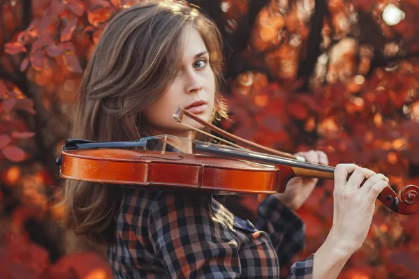 Mujer joven con violín rojo y arco sobre un fondo de naturaleza otoñal, chica romántica dedicada al arte musical, un concepto de hobby, concierto al aire libre — Foto de Stock