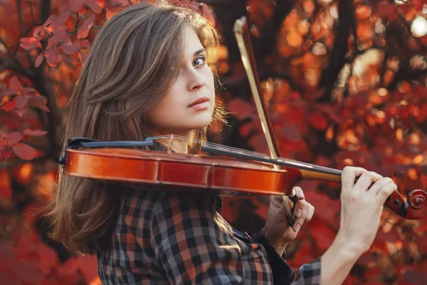 Mujer joven con violín rojo y arco sobre un fondo de naturaleza otoñal, chica romántica dedicada al arte musical, un concepto de hobby, concierto al aire libre — Foto de Stock