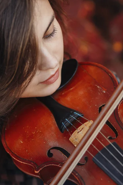 Cara de mujer hermosa disfrutando de tocar el violín sobre un fondo de hojas rojas de otoño, chica romántica dedicada al arte en la naturaleza, concepto de hobby, vista superior — Foto de Stock