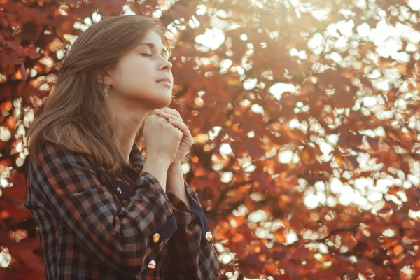 Portrait d'une jeune femme priant dans la nature, la jeune fille remercie Dieu avec ses mains pliées à son menton, une conversation avec le Créateur, le concept de religion — Photo