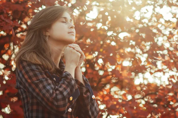 Portret van een jonge vrouw die in de natuur bidt, het meisje dankt God met haar handen gevouwen op haar kin, een gesprek met de Schepper, het begrip religie — Stockfoto