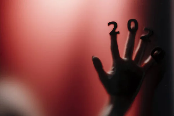 Silhouette of a female hand with date on fingers pressed to glass of door with a red strange backlight, destruction of the stereotype happy new year, entering 2020 horror genre — Stock fotografie