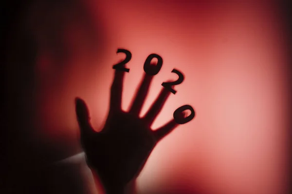Sziluett egy női kéz dátum ujjak préselt üveg ajtó piros furcsa háttérvilágítással, megsemmisítése a sztereotípia boldog új évet, belépő 2020 horror műfaj — Stock Fotó