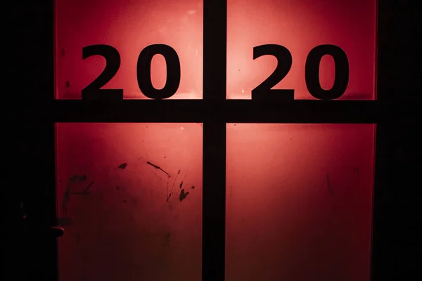 Silhouette date 2020 in piedi sulla porta contro una strana retroilluminazione rossa, concetto nuovo anno e paura del futuro — Foto Stock