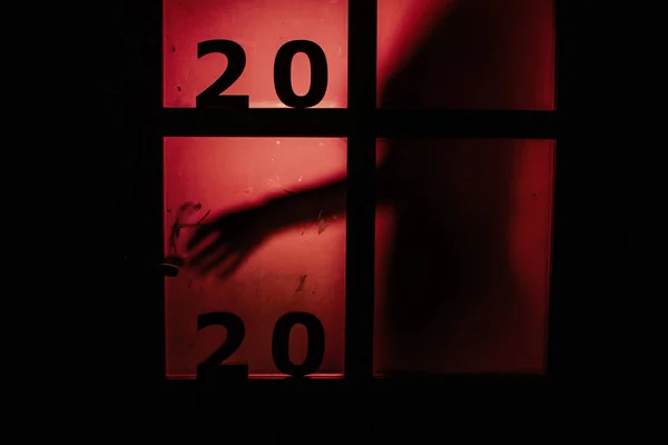 Silhouette of a person opening the door handle with date on window with a red strange backlight, destruction of the stereotype happy new year, entering 2020 horror genre — Stock Photo, Image