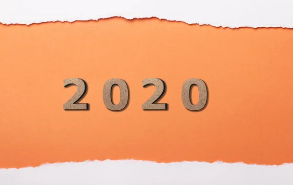 Data con figura in legno 2020 sotto una striscia strappata di cartone bianco, numeri in buco arancione di carta strappata, concetto di anno nuovo, disegno della copertina del calendario — Foto Stock