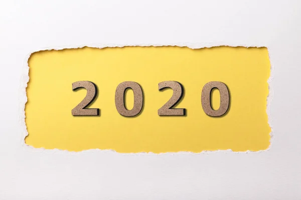 Fond blanc avec la figure en bois de la date 2020 dans le trou jaune de carton déchiré, concept de nouvelle année, conception de couverture de calendrier — Photo