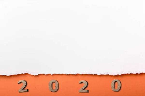 Fecha con figura de madera 2020 bajo una tira rasgada de cartón blanco, números en agujero naranja de papel rasgado, concepto de año nuevo, diseño de la cubierta del calendario — Foto de Stock
