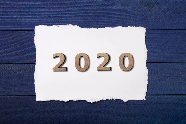 Chiffres 2020 disposés sur un morceau de carton blanc sur un fond en bois bleu, concept nouvelle année, calendrier design — Photo
