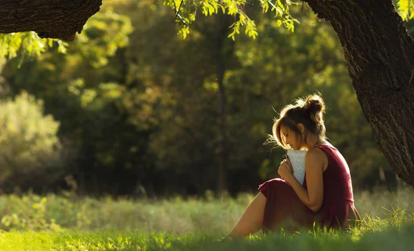 Sonniges Porträt eines schönen Mädchens, das auf einer grünen Lichtung unter Ästen mit Buch sitzt, Frau liest Roman über Natur, Konzept Hobby und Lifestyle — Stockfoto