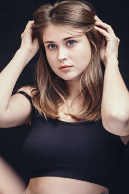 Siyah arka planda güzel bir kızın portresi, spor bir bluzla, romantik genç bir kadın aynada kendine hayran, saç stili deniyor, doğal güzellik kavramı, modellik işi.