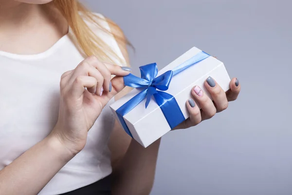 Mujer manos apertura caja de regalo en un fondo de estudio, hembra desatando lazo azul, vacaciones concepto — Foto de Stock