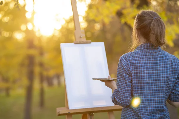 young woman artist drawing a picture on canvas on an easel in nature, a girl with a brush and a palette of paints working inspired by early autumn, a concept of art, hobby