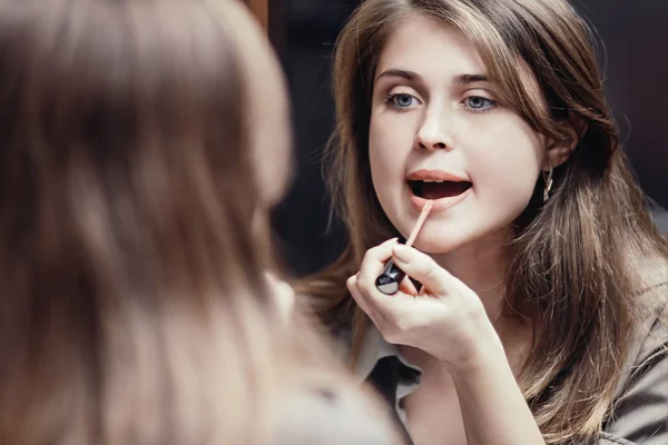 Girl paints her lips with lipstick in front of a mirror at home, a young woman doing makeup, a concept of female natural beauty and cosmetics — Stock Photo, Image