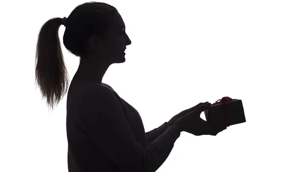 Silhouette di una giovane donna che dà regalo in mano, ragazza con una scatola con un fiocco su uno sfondo bianco isolato, concetto di vacanze — Foto Stock