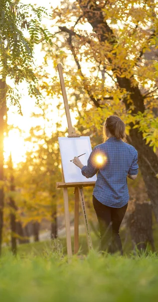 Young woman artist drawing a picture on canvas on an easel in nature, a girl with a brush and a palette of paints working inspired by early autumn, a concept of art, hobby — 스톡 사진