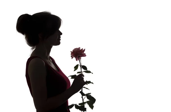 Silhouette d'une jeune femme heureuse dans une robe et avec une rose dans les mains, figure de belle fille mince avec une fleur sur un fond blanc isolé — Photo