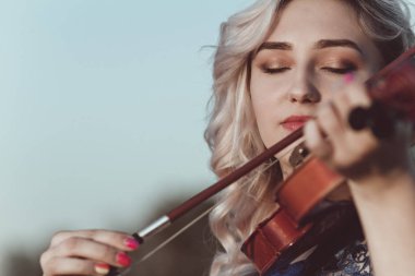 Güzel bir kızın yüzü, çenesinin altında bir kemanla, romantik genç bir kadın yalnızlık, konsept müzik ve duygularla doğada müzik aleti çalıyor.