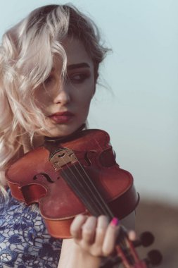 Çenesinin altında keman olan güzel bir kızın yüzü, yalnızlık, konsept müzik ve duygular üzerine müzik aleti çalan genç bir kadın.