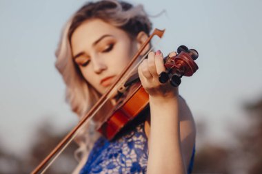 Güzel bir kızın yüzü, çenesinin altında bir kemanla, romantik genç bir kadın yalnızlık, konsept müzik ve duygularla doğada müzik aleti çalıyor.